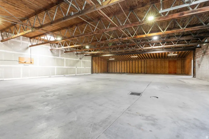 Expansive open industrial space featuring a concrete floor, exposed wood beam ceiling, metal truss system, and recessed lighting