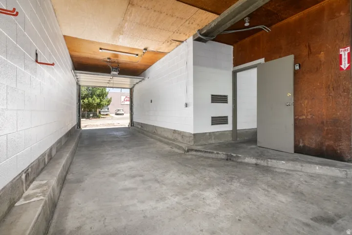 Concrete floor garage with high ceilings, an overhead garage door, interior metal door, and block wall construction