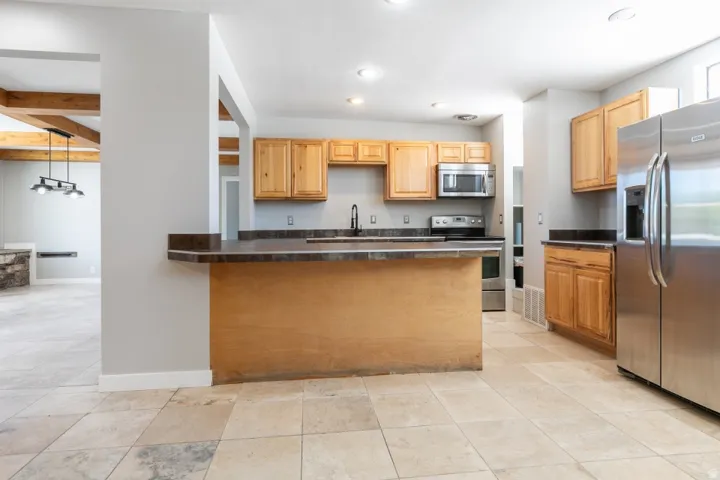 Kitchen with light wood cabinetry, dark countertops, and stainless steel appliances