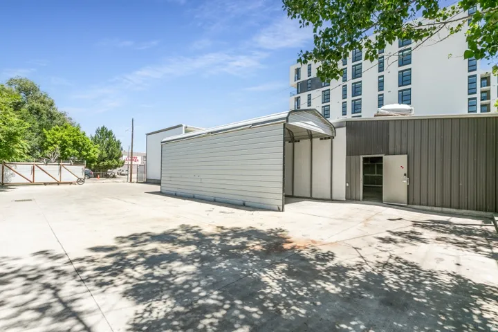 Expansive concrete pad featuring a metal carport structure and a corrugated metal building with an open doorway