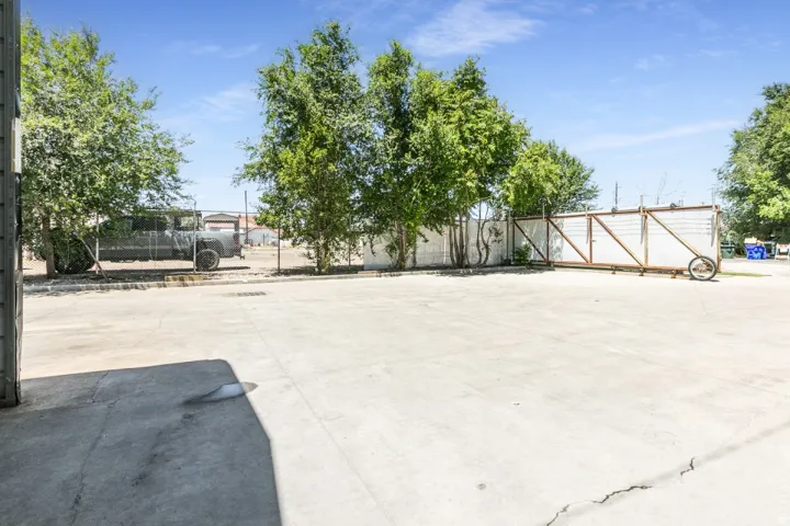 Expansive concrete lot with a chain-link fence and mature trees