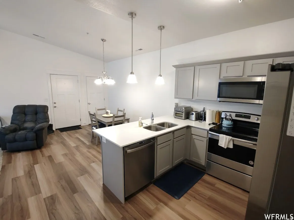 Contemporary kitchen with light gray cabinetry, stainless steel appliances, white countertops, and wood-finish flooring