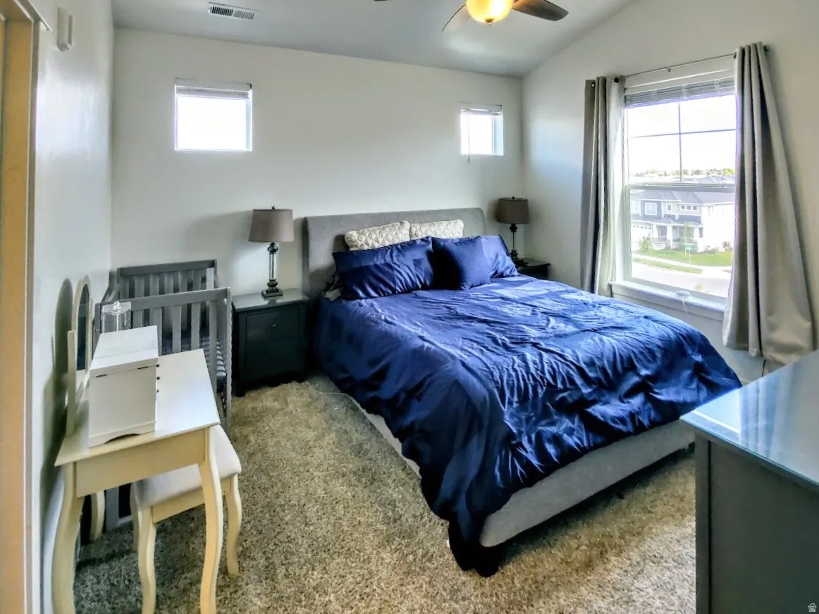 Bright bedroom featuring a vaulted ceiling with a built-in ceiling fan, light-colored walls, multiple windows for natural illumination, and carpet flooring