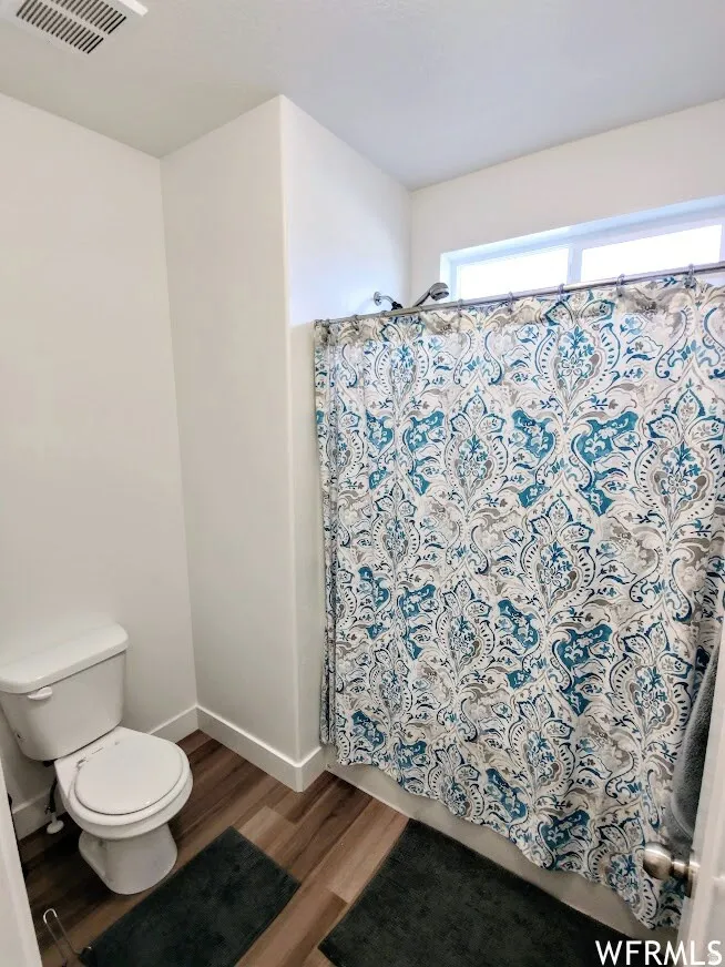 Bathroom featuring wood-finish flooring, a white toilet, and white walls