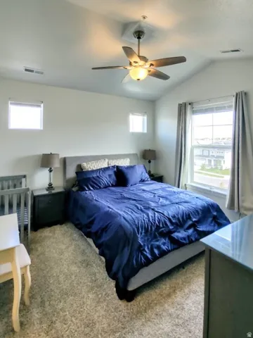 Carpeted room featuring a ceiling fan with integrated lighting, a vaulted ceiling, and multiple windows