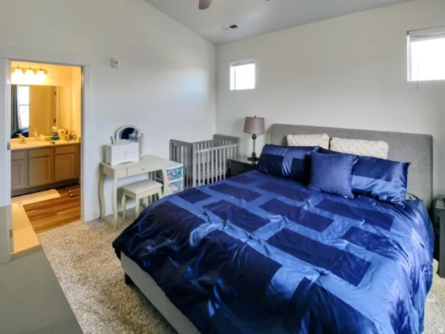 Spacious bedroom featuring light-colored walls, carpet flooring, and two high-set windows providing natural light