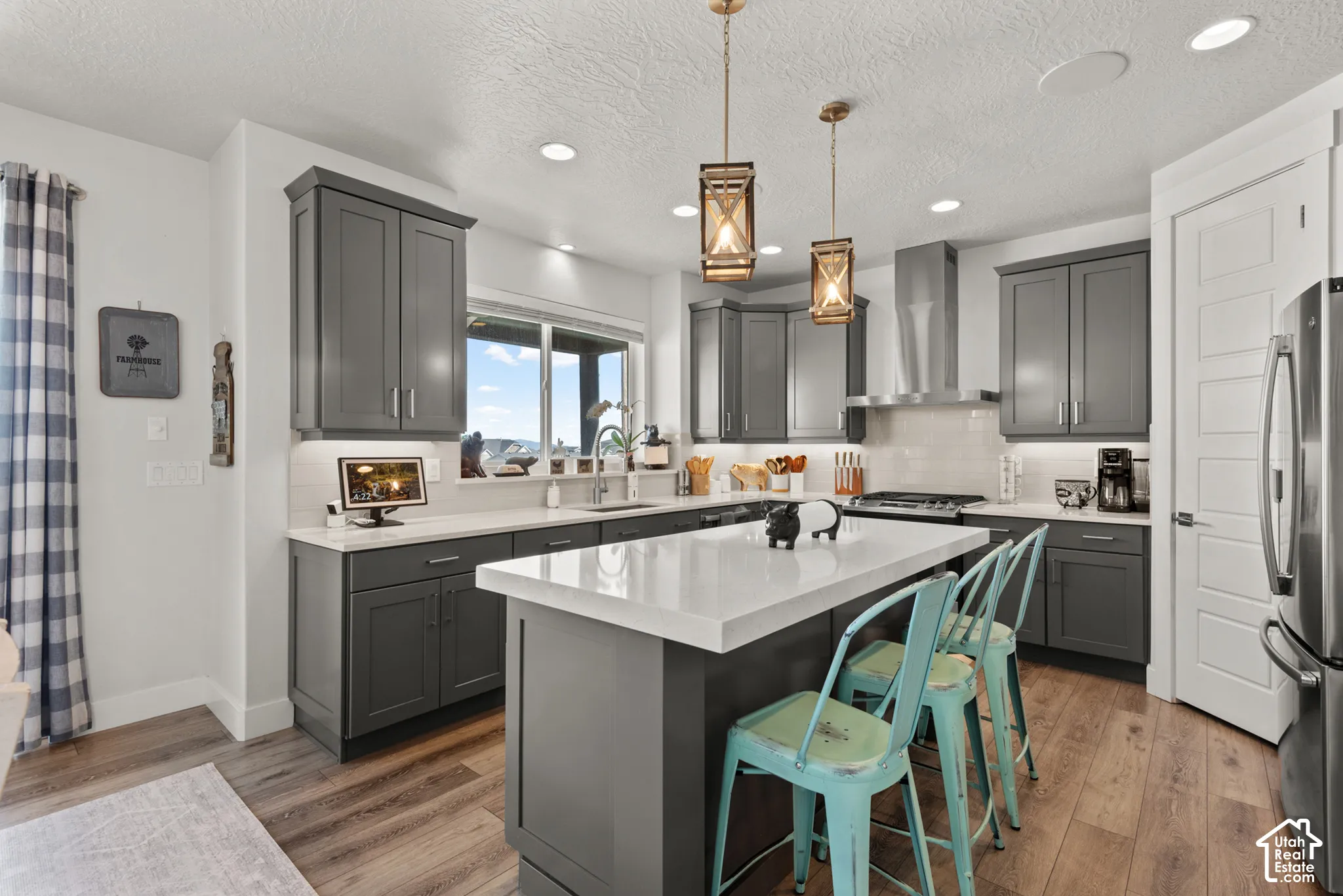 Contemporary kitchen featuring dark gray cabinetry, white countertops, stainless steel appliances, and wood-finish flooring