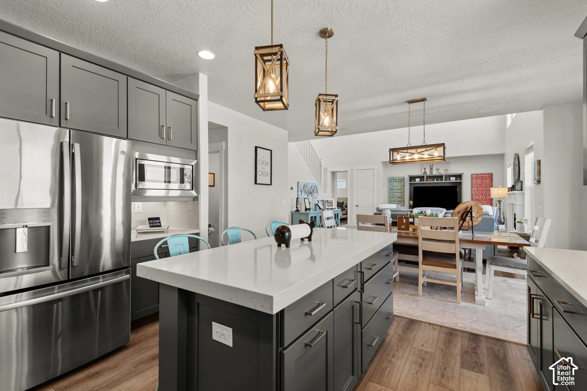 Kitchen featuring a spacious island with a light-toned countertop, gray cabinetry, stainless steel appliances, wood-finish flooring, and pendant lighting