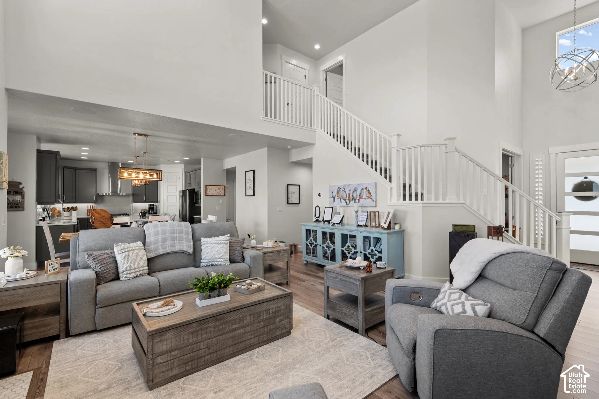 Open-concept living space featuring high ceilings, wood-finish flooring, a two-story staircase with white railings, and an overhead lighting fixture