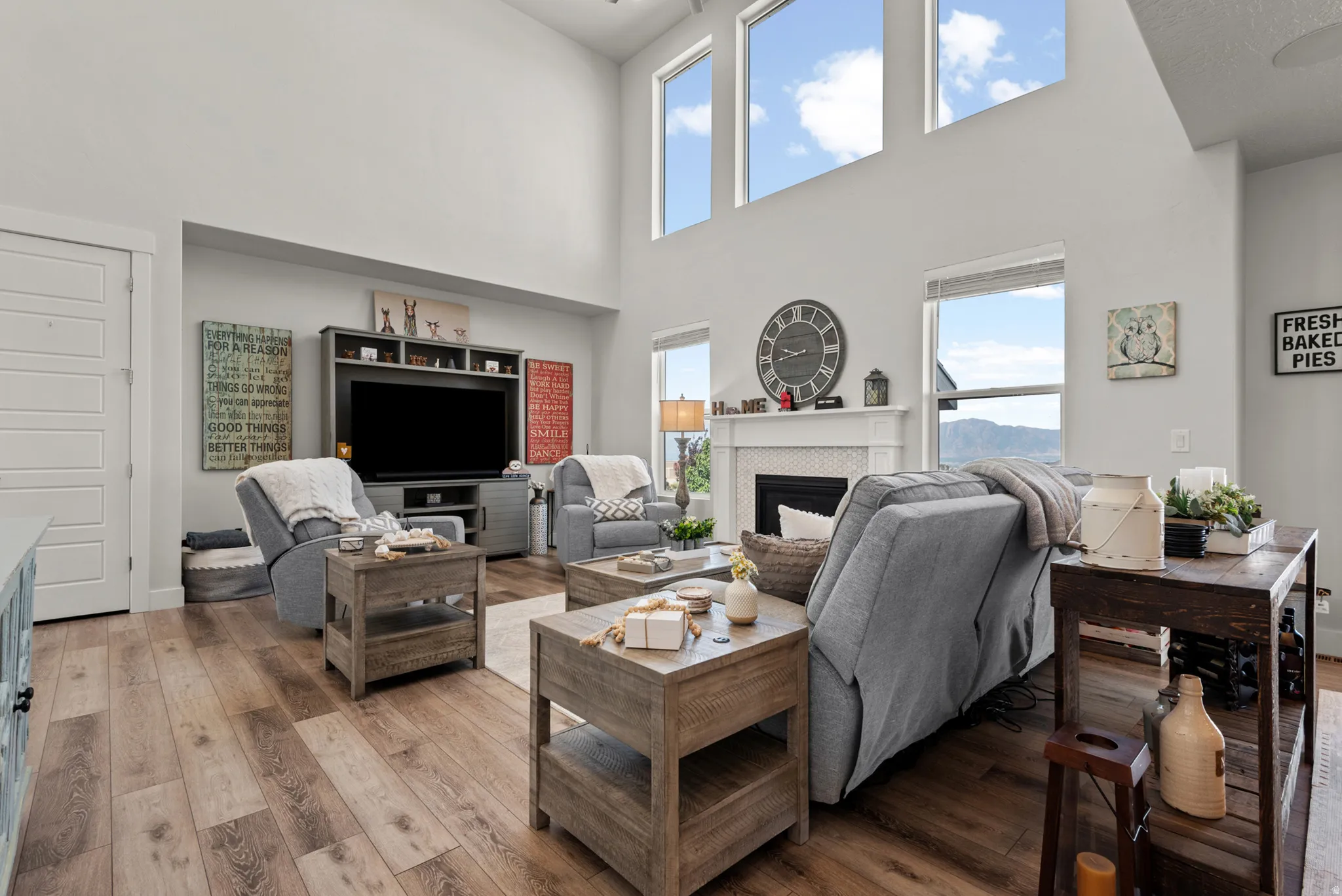 Living area featuring high ceilings, wood-finish flooring, a white fireplace with a textured tile surround, built-in shelving, and multiple large windows
