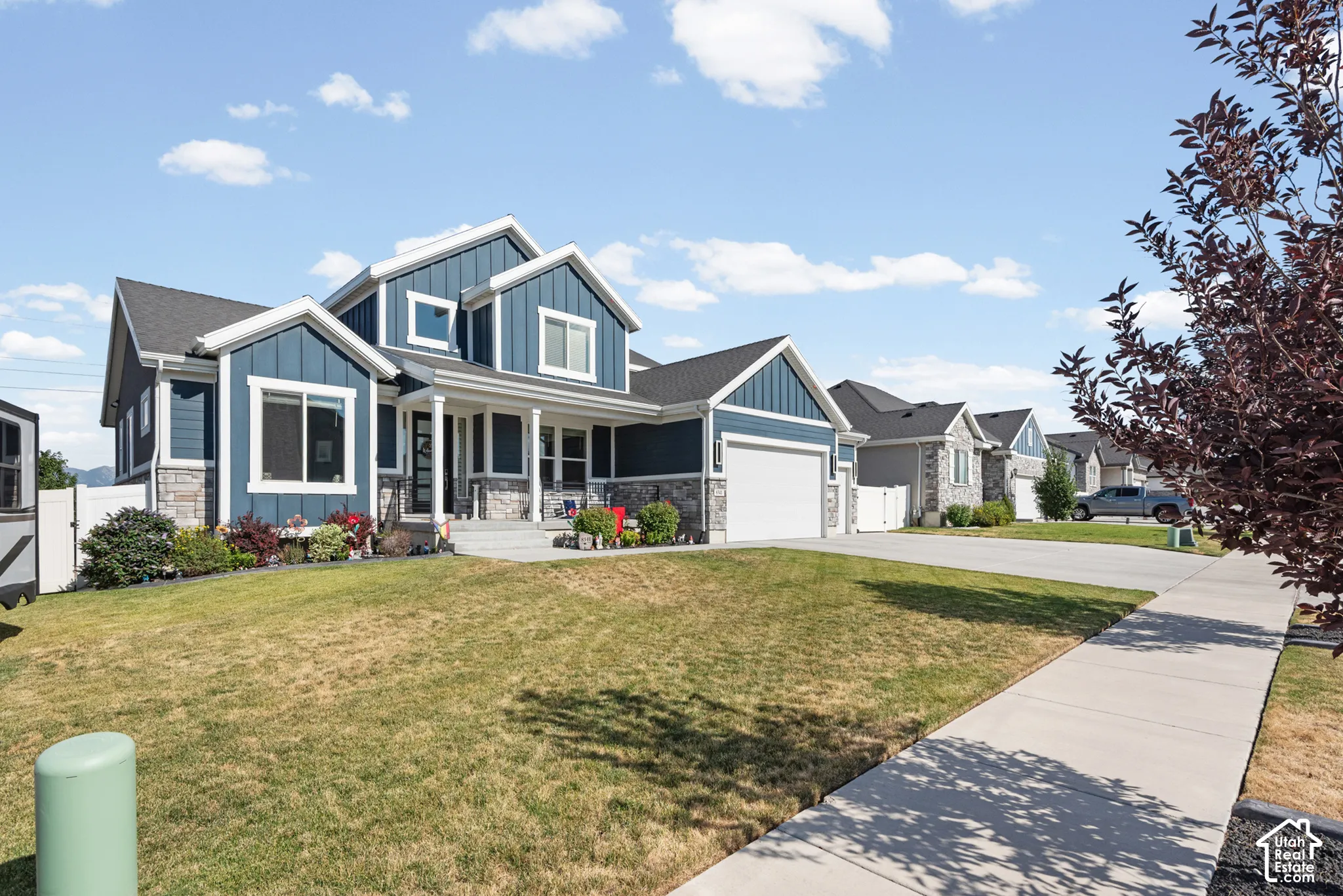 Contemporary residence featuring a two-car garage, dark-toned siding with stone accents, a covered front porch, and a concrete driveway