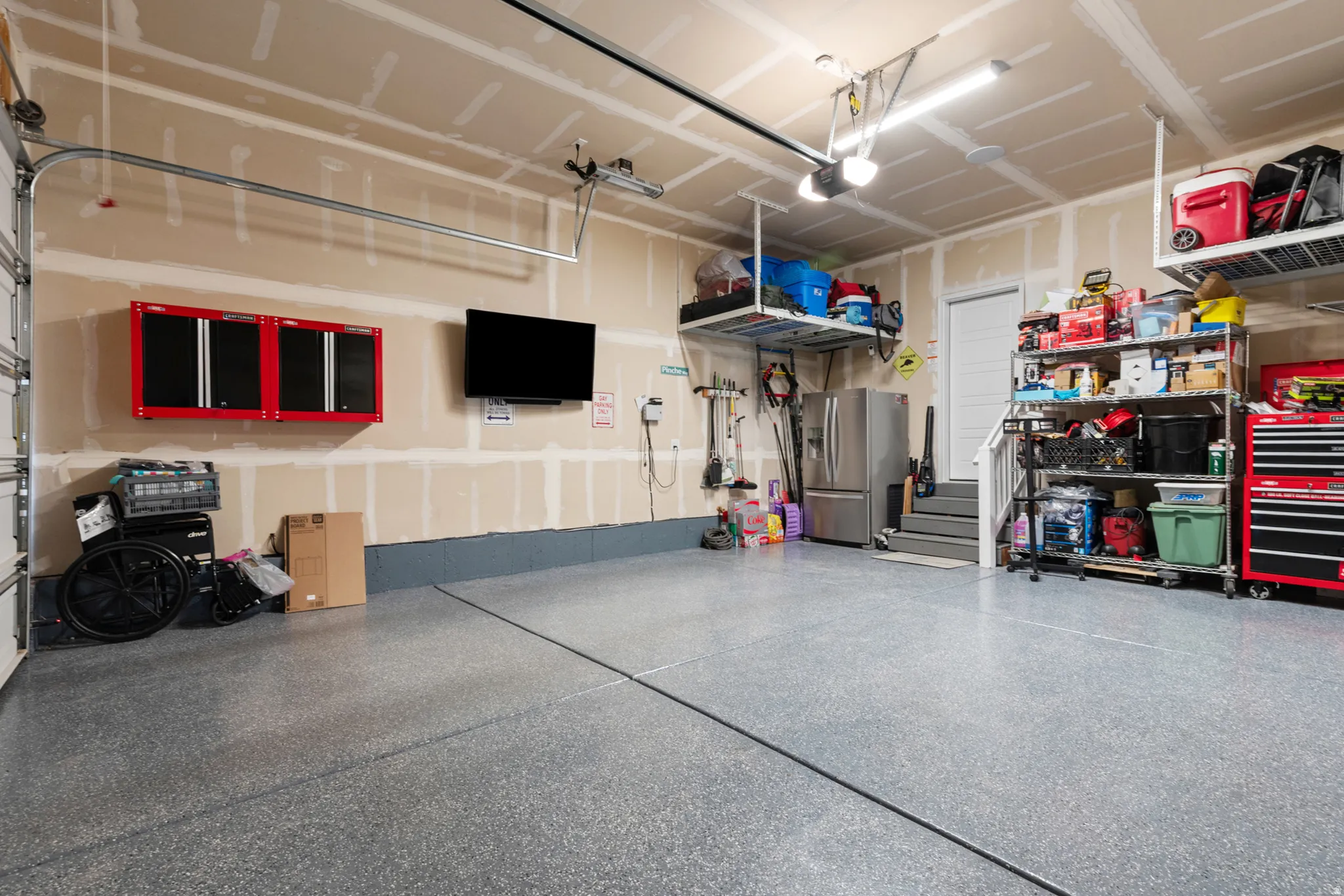 Spacious garage featuring a durable epoxy floor coating, overhead storage racks, fluorescent lighting, and wall-mounted cabinetry