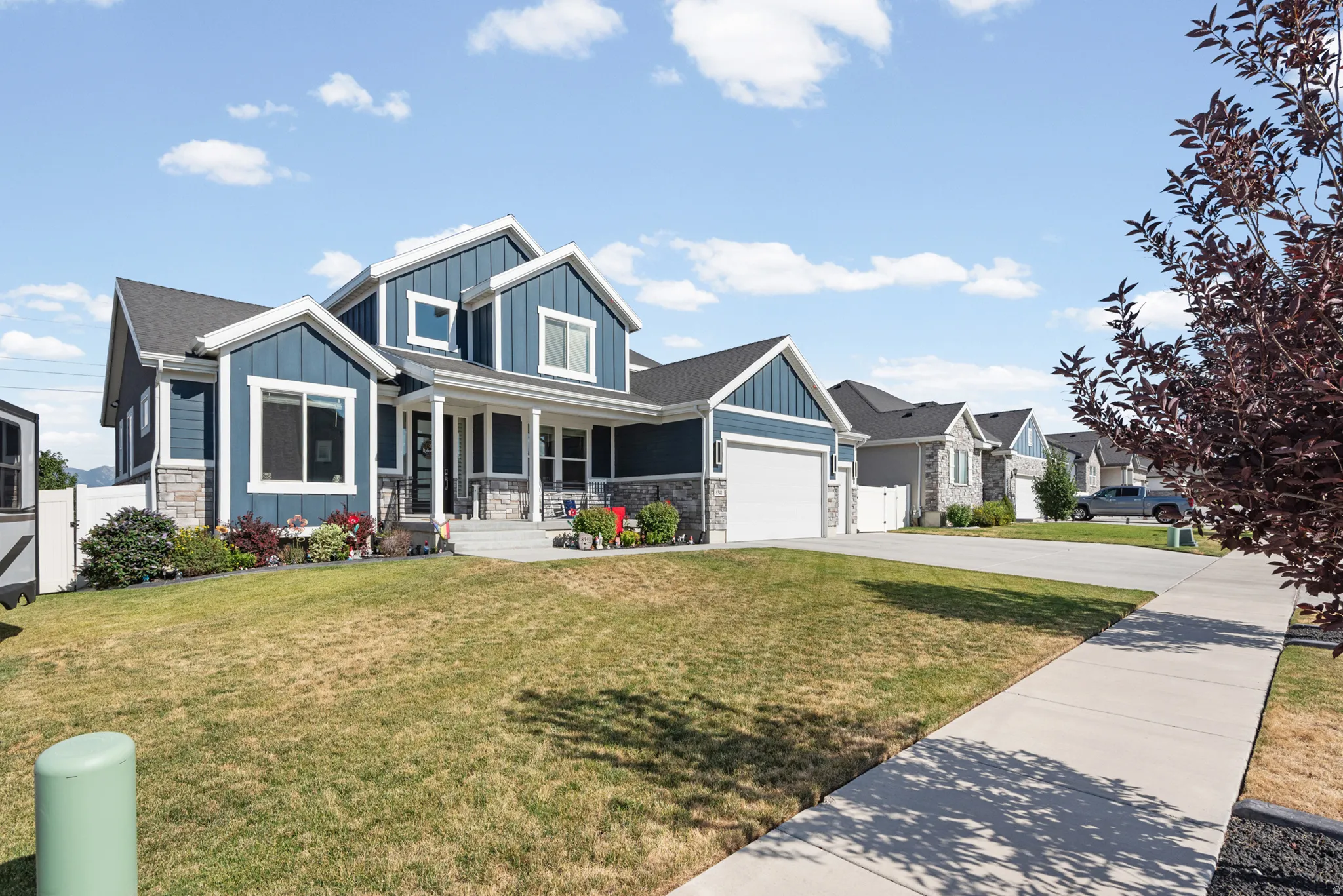 Contemporary residence featuring a two-car garage, dark-toned siding with stone accents, a covered front porch, and a concrete driveway