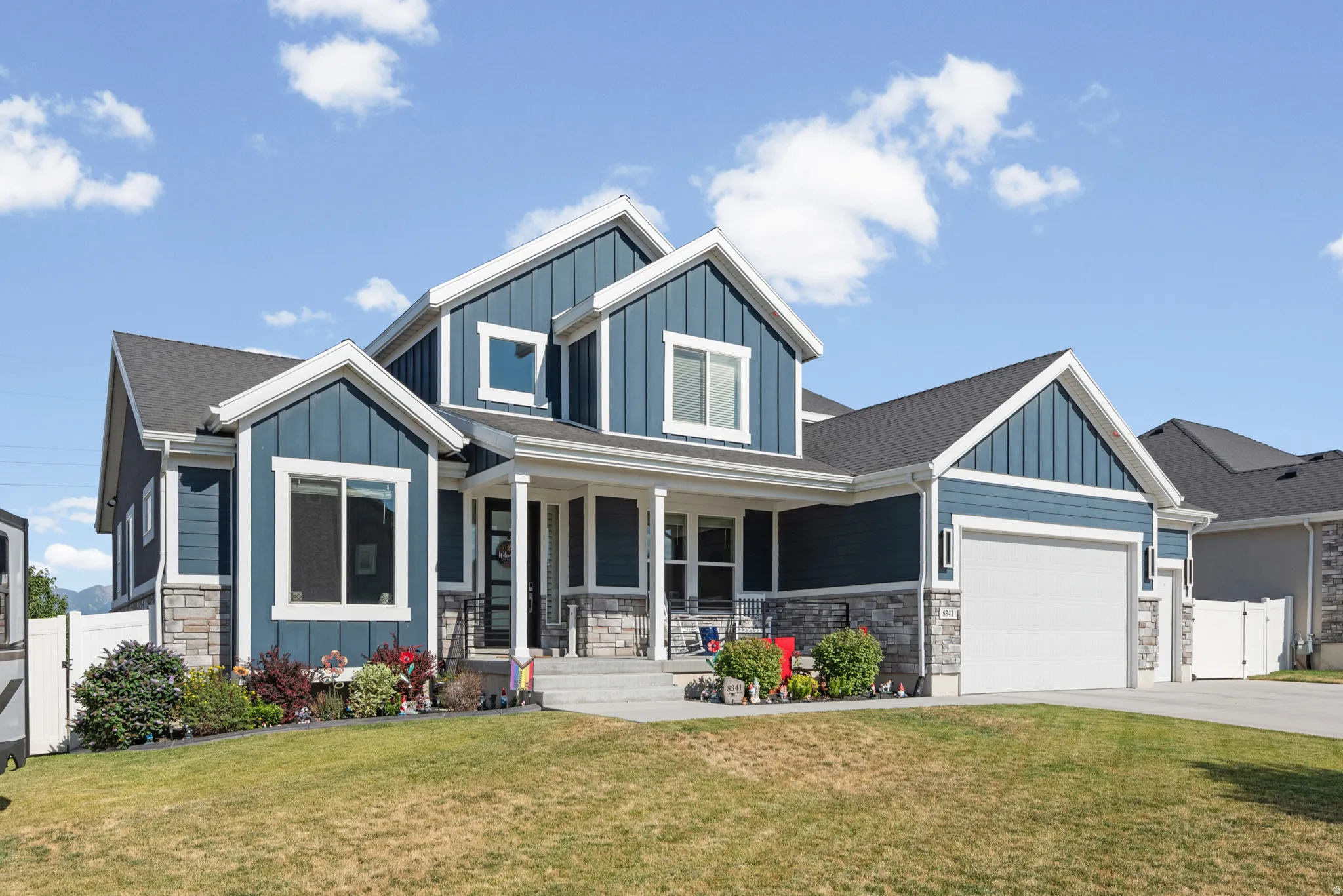 Contemporary residence featuring a striking blue exterior with board and batten and horizontal siding, stone accents, a covered front porch, and an attached two-car garage