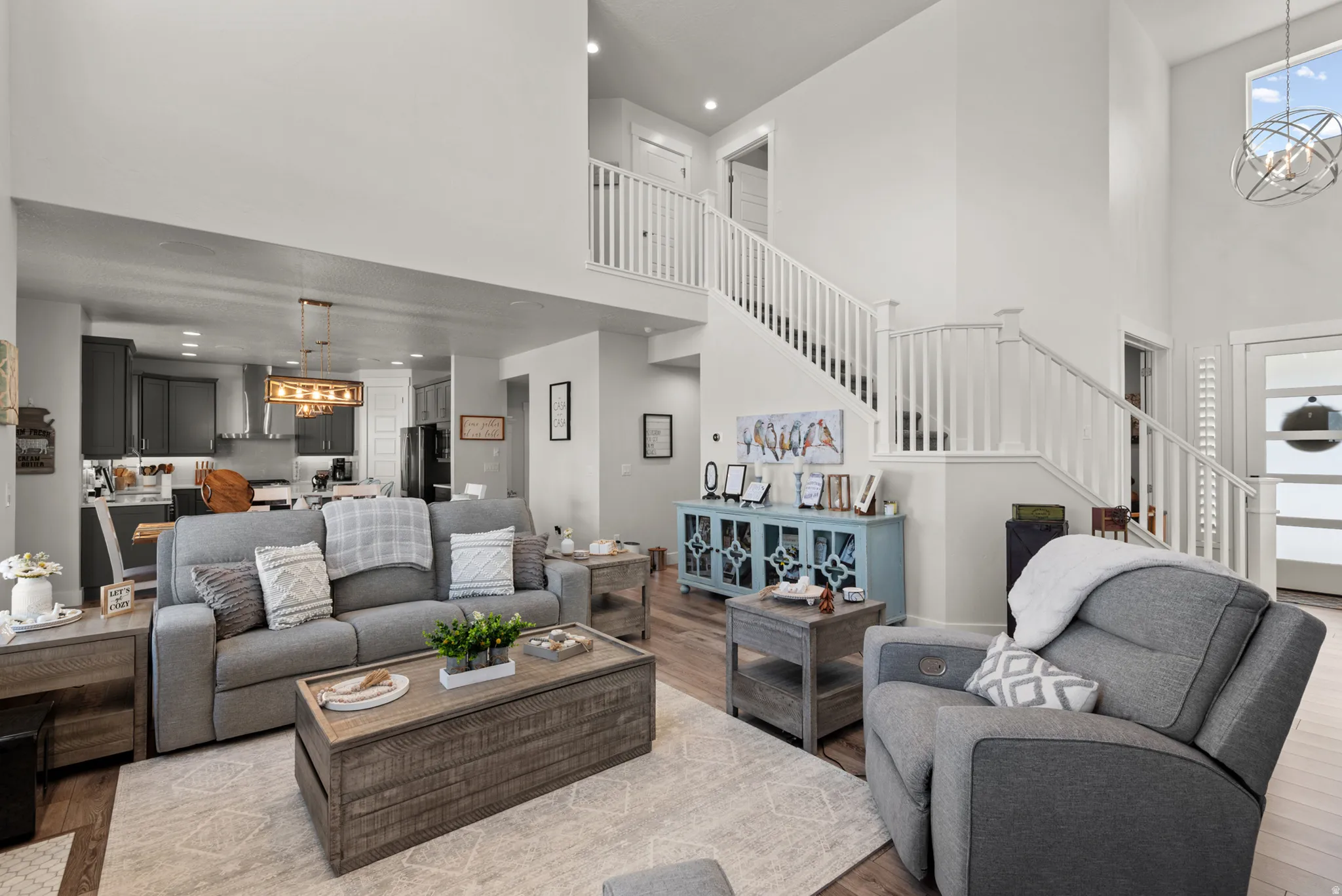 Open-concept living space featuring high ceilings, wood-finish flooring, a two-story staircase with white railings, and an overhead lighting fixture