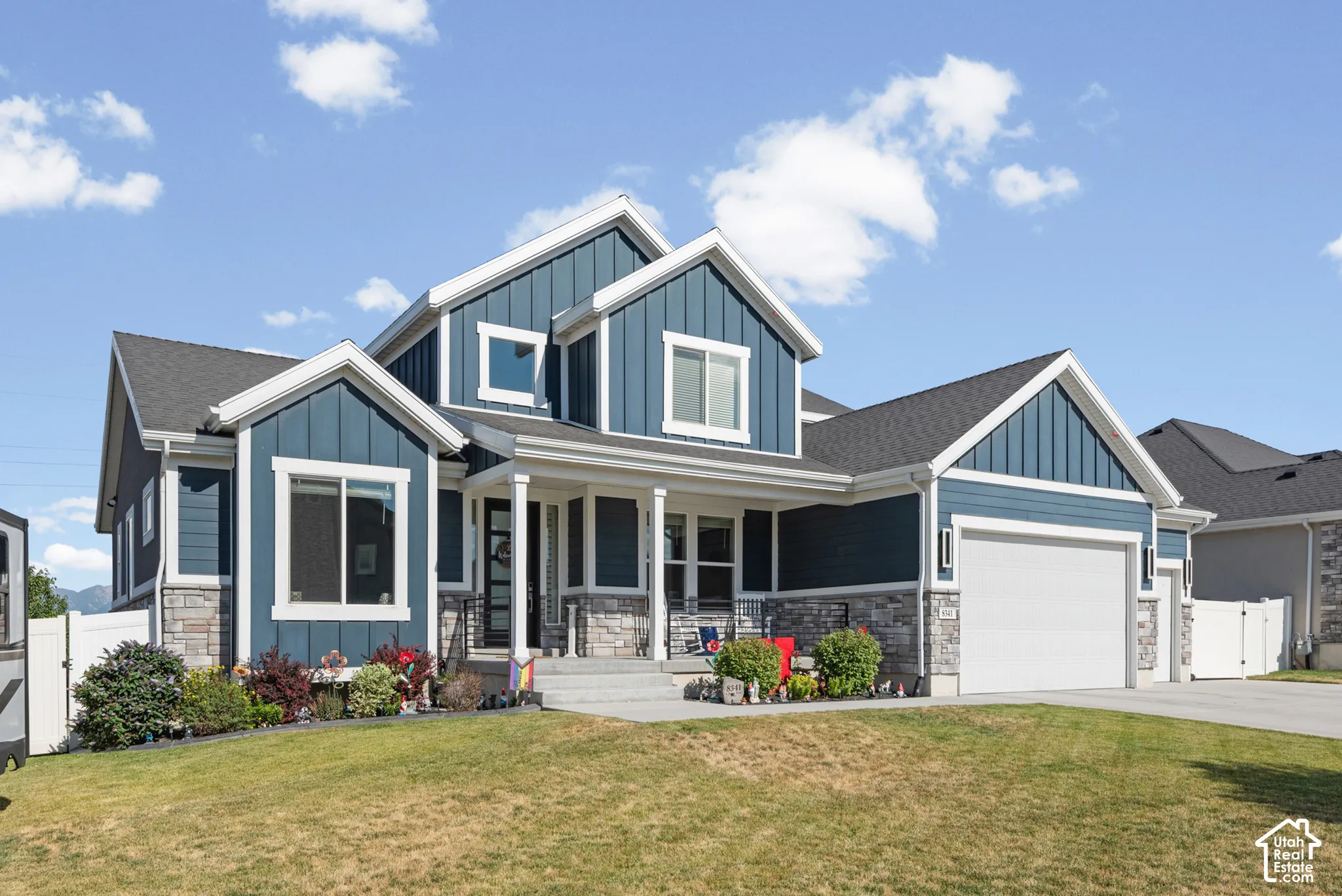 Contemporary residence featuring a striking blue exterior with board and batten and horizontal siding, stone accents, a covered front porch, and an attached two-car garage