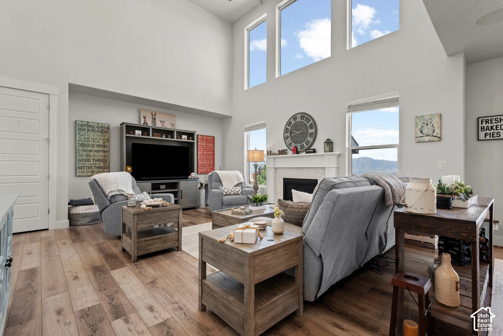 Living area featuring high ceilings, wood-finish flooring, a white fireplace with a textured tile surround, built-in shelving, and multiple large windows