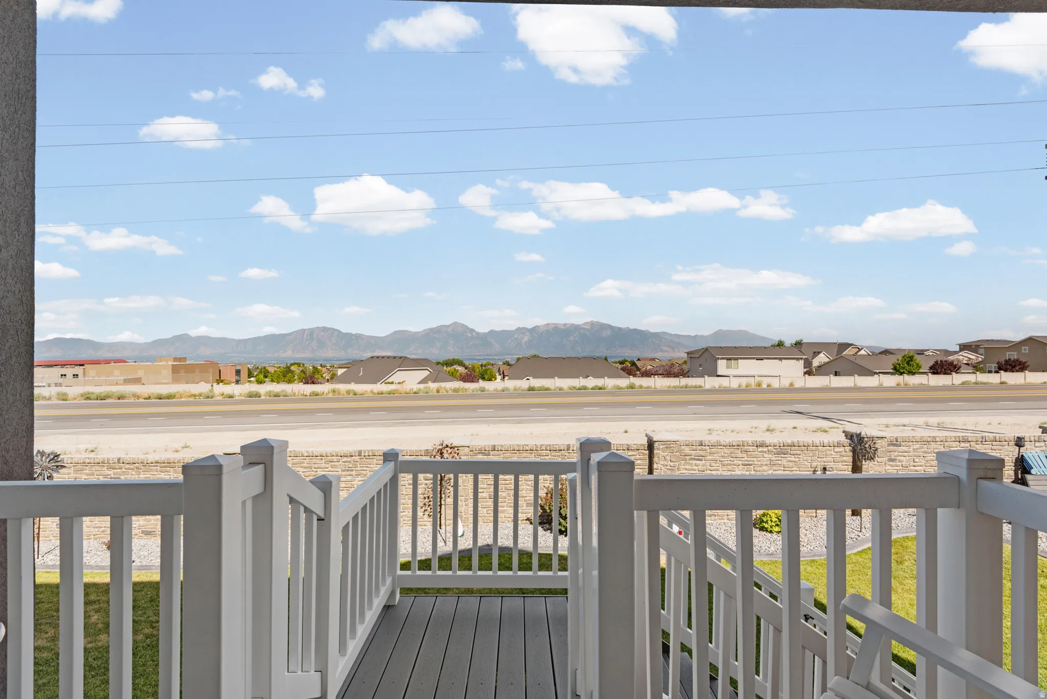 Outdoor deck area featuring composite decking and white railing, with distant mountains and residential structures visible