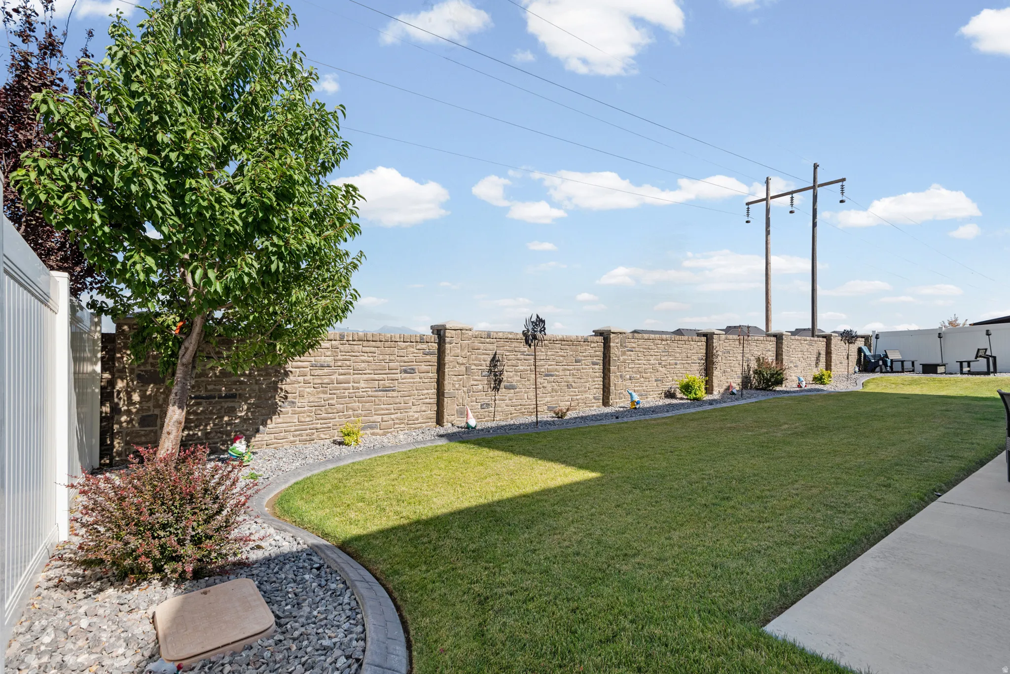 Expansive yard featuring a manicured lawn, a stone-faced perimeter wall, and a white vinyl privacy fence