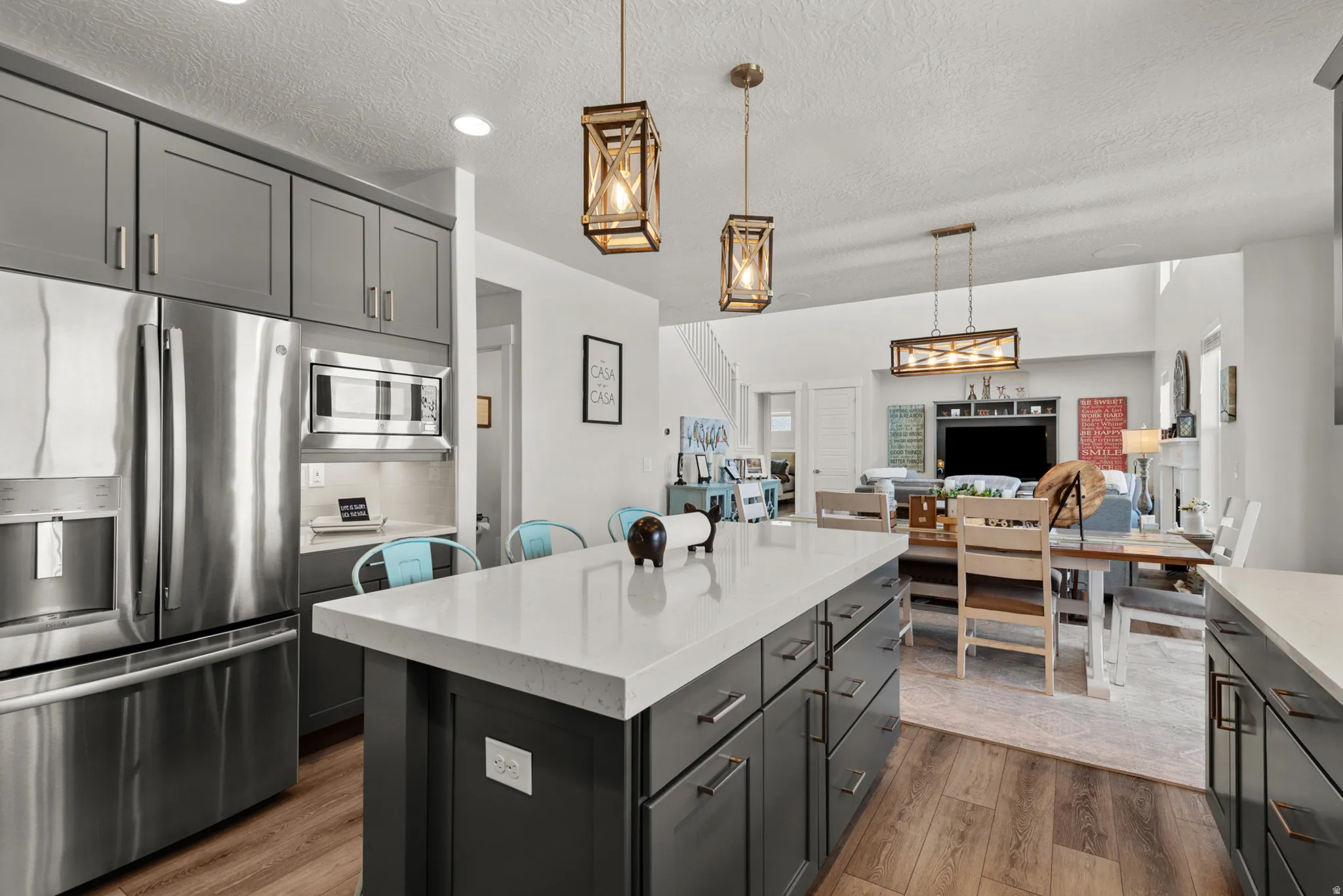 Kitchen featuring a spacious island with a light-toned countertop, gray cabinetry, stainless steel appliances, wood-finish flooring, and pendant lighting
