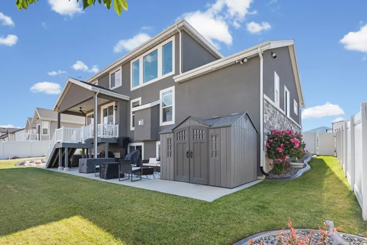 Rear exterior featuring a covered deck with white railings, a ground-level patio, a storage shed, and a stone facade accent