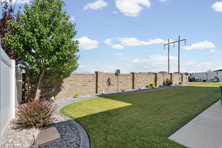 Expansive yard featuring a manicured lawn, a stone-faced perimeter wall, and a white vinyl privacy fence