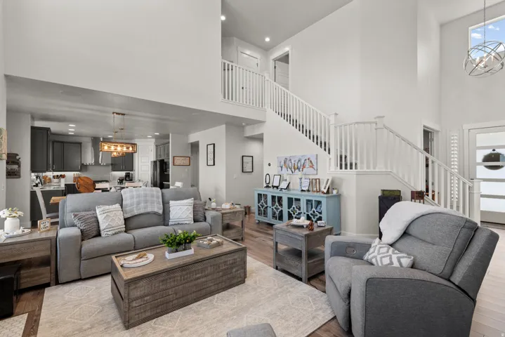 Open-concept living space featuring high ceilings, wood-finish flooring, a two-story staircase with white railings, and an overhead lighting fixture