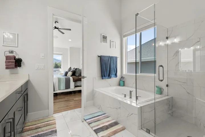 Bathroom featuring a built-in soaking tub, glass-enclosed shower, white tile flooring, and white and gray marbled wall tiling