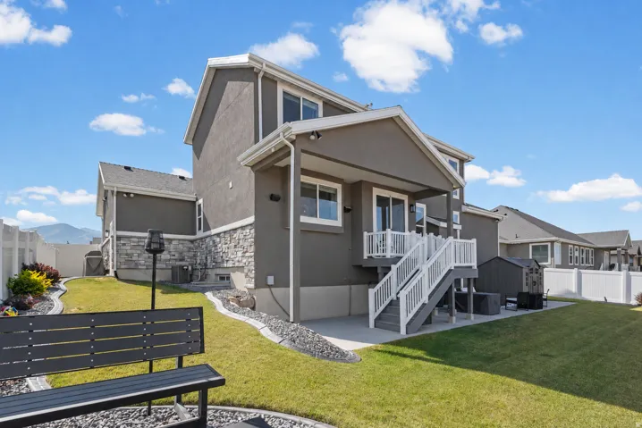 Rear exterior featuring a covered patio, a walk-out deck with white railings, and a manicured lawn