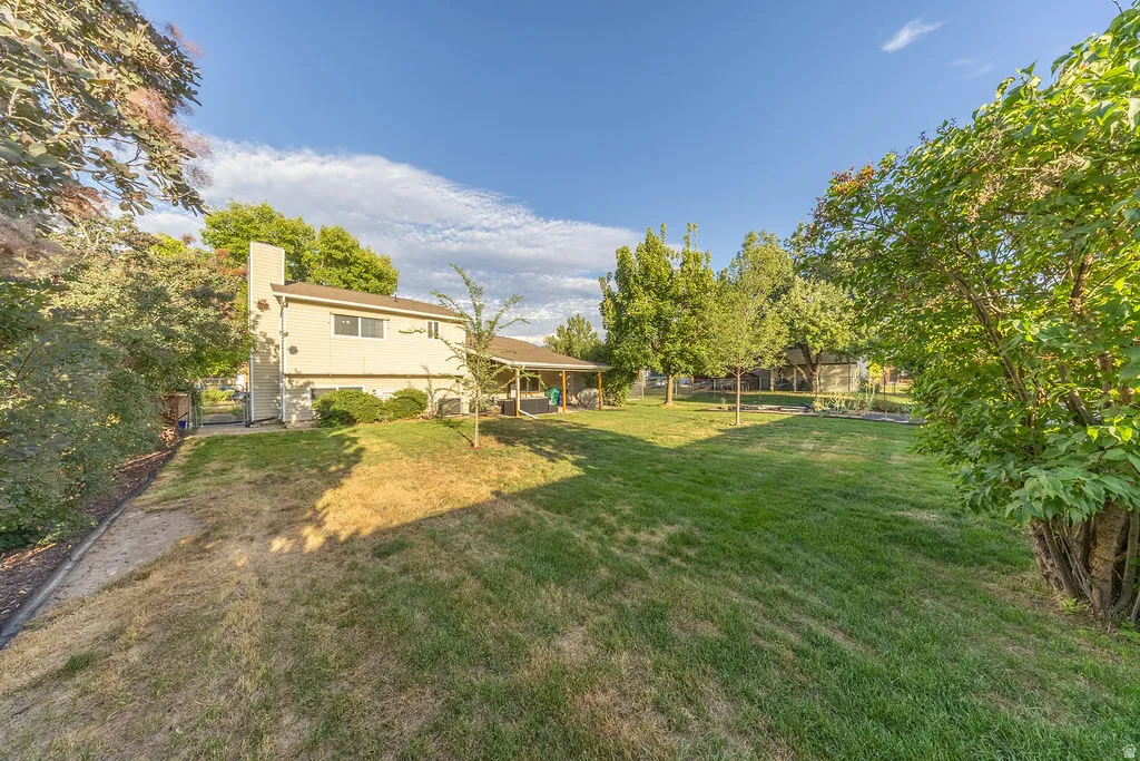 Expansive backyard featuring a manicured lawn, established trees, and a covered patio
