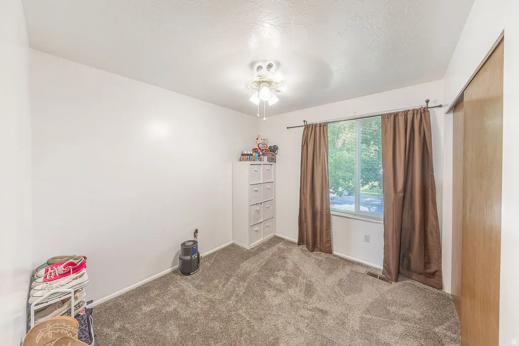 Carpeted room featuring a window with exterior views, a ceiling fan with integrated lighting, and a sliding wood-finish closet door