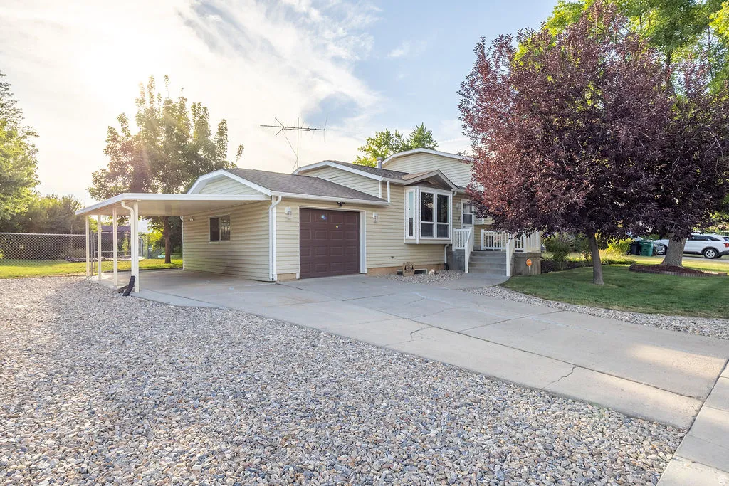 Exterior featuring light-toned siding, an attached garage with a brown door, and a carport