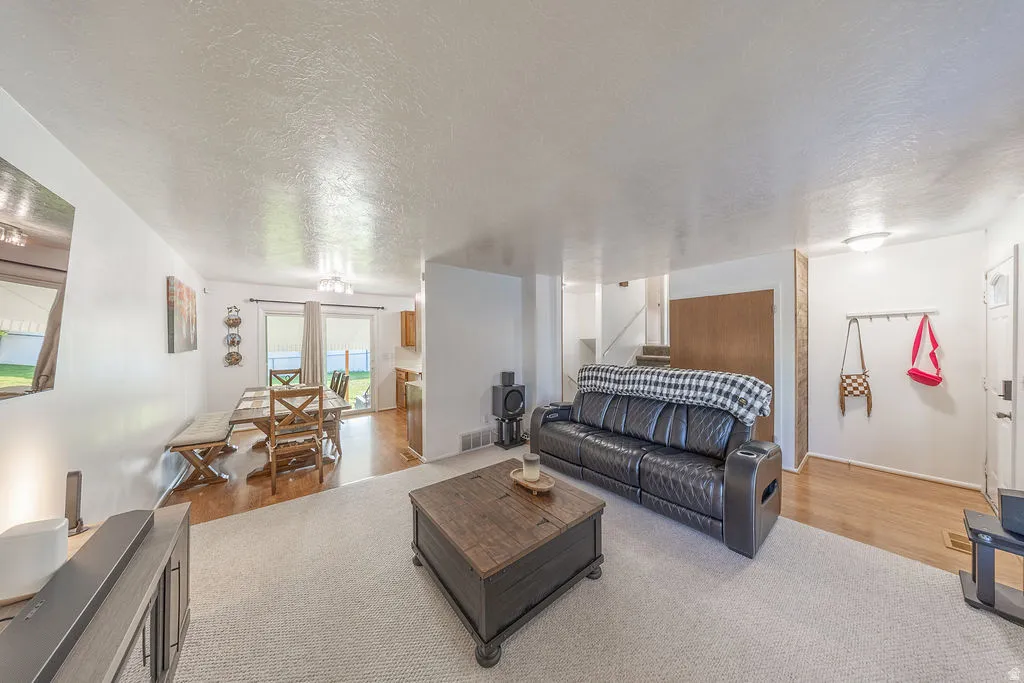 Open-concept living area featuring a neutral carpeted zone, wood-finish flooring in the dining space, and a dining area with direct outdoor access via sliding glass doors