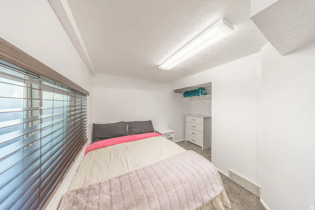 Bedroom featuring a window with horizontal blinds, overhead fluorescent lighting, and wall-to-wall carpeting