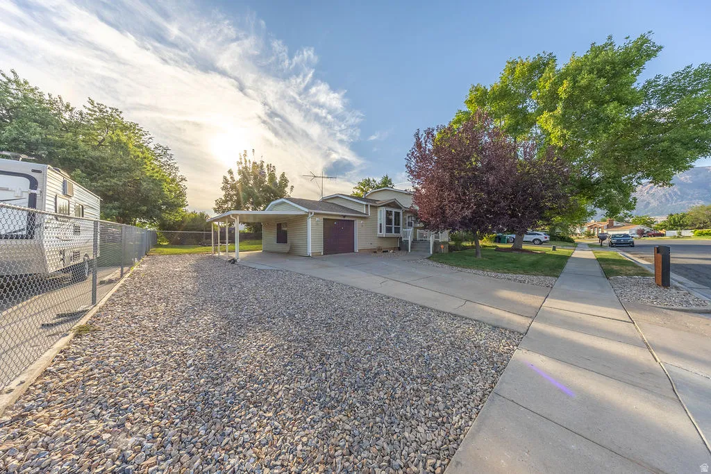 Single-story residence featuring a two-car garage, an additional carport, and a gravel side yard with chain link fencing