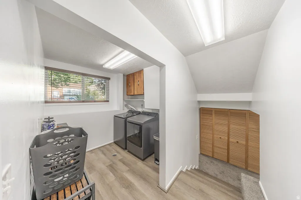 Dedicated laundry area featuring a window, overhead cabinetry, and wood-finish flooring