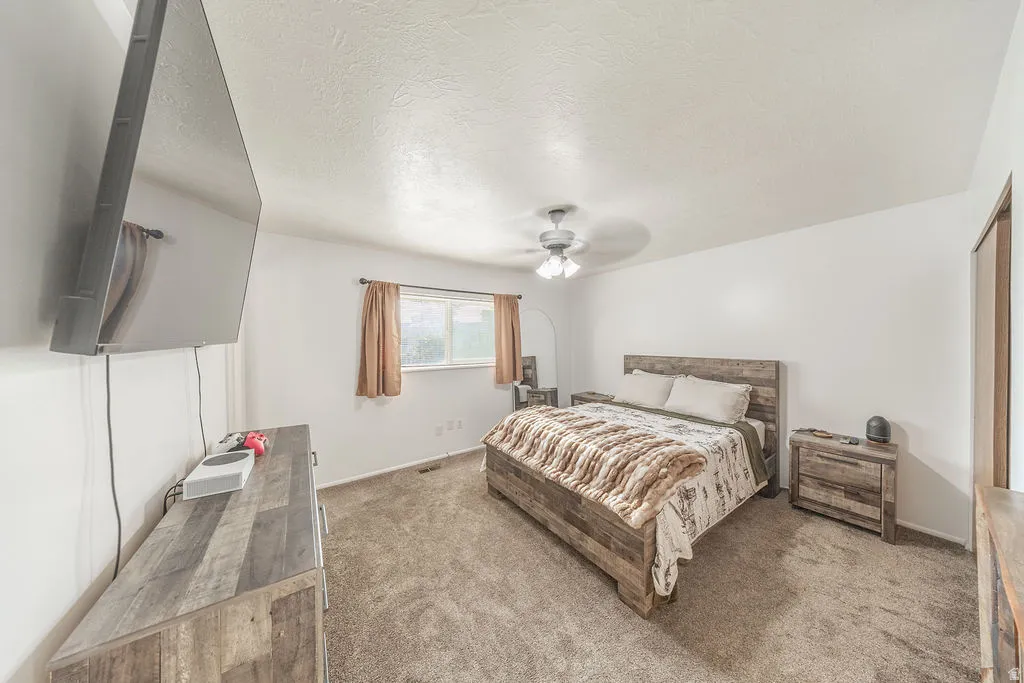 Carpeted bedroom featuring a ceiling fan with light fixture, window with curtains, and a built-in closet with wood-finish door