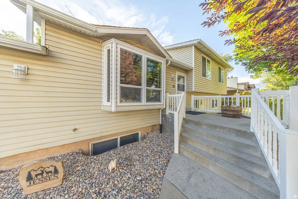 Exterior featuring light beige siding, a large bay window, and a concrete patio