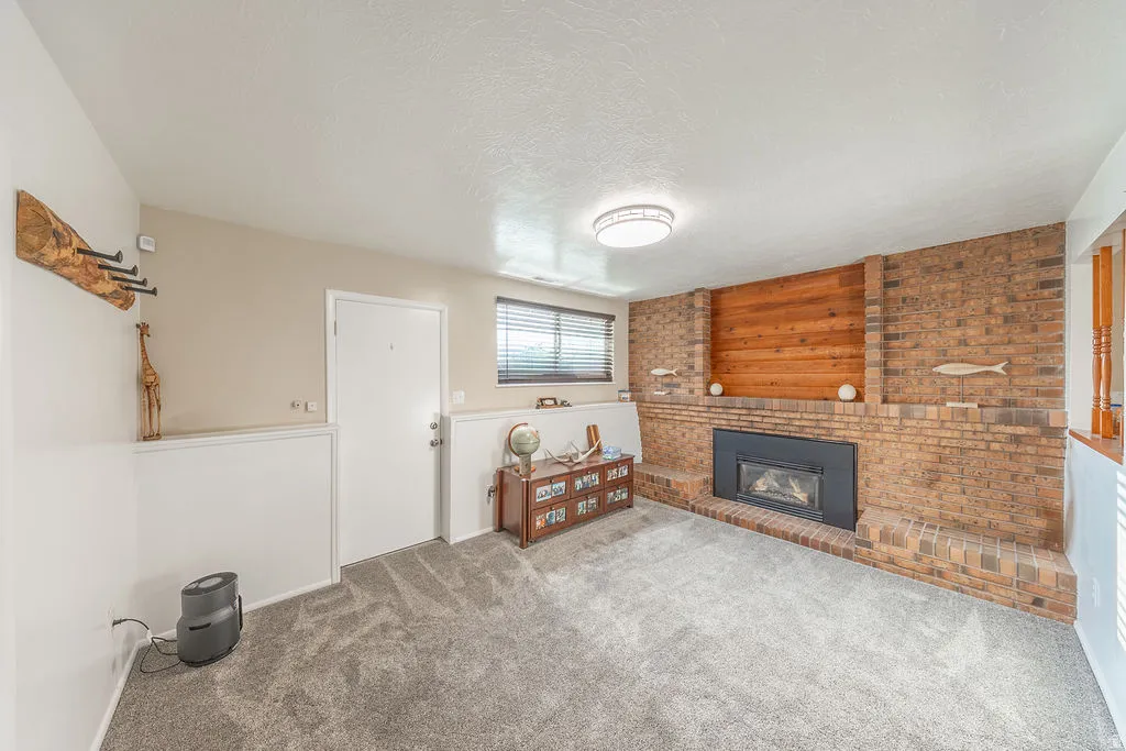 Living area featuring a brick fireplace with a black insert, wood paneling, plush gray carpeting, and a ceiling-mounted light fixture