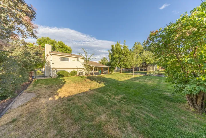 Expansive backyard featuring a manicured lawn, established trees, and a covered patio