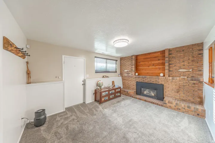 Living area featuring a brick fireplace with a black insert, wood paneling, plush gray carpeting, and a ceiling-mounted light fixture