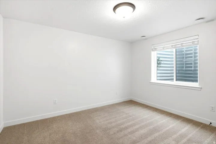 Bright room featuring neutral carpet flooring, a window with blinds, white trim, and a flush-mount ceiling light fixture