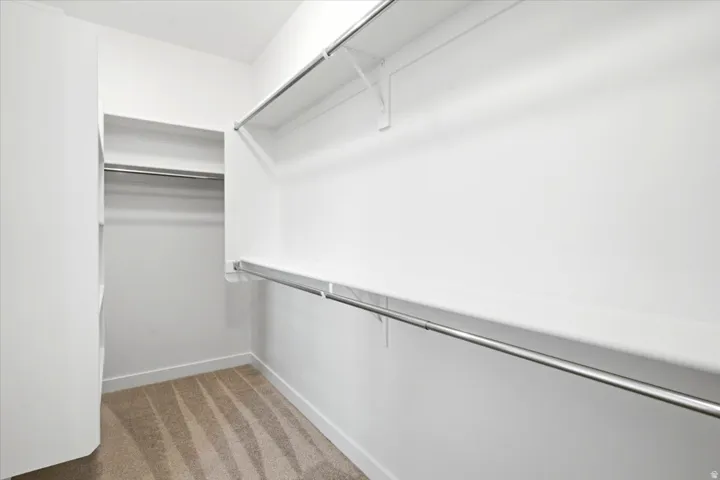 Walk-in closet featuring white walls, white shelving, metal hanging rods, and patterned carpeting
