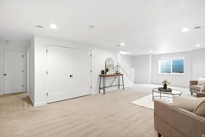 Spacious lower-level living area featuring neutral carpeting, recessed lighting, and a white staircase with matching railing