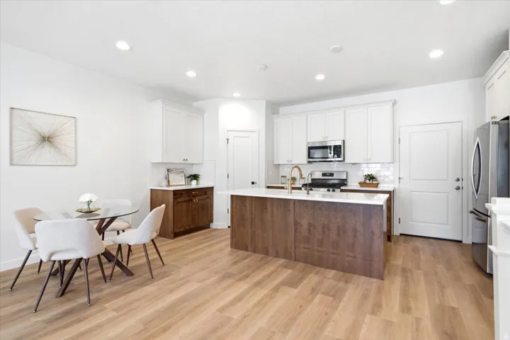 Open-concept kitchen and dining area featuring light wood-finish flooring, white cabinetry, a wood-finish island with a light-toned countertop, stainless steel appliances, and recessed lighting