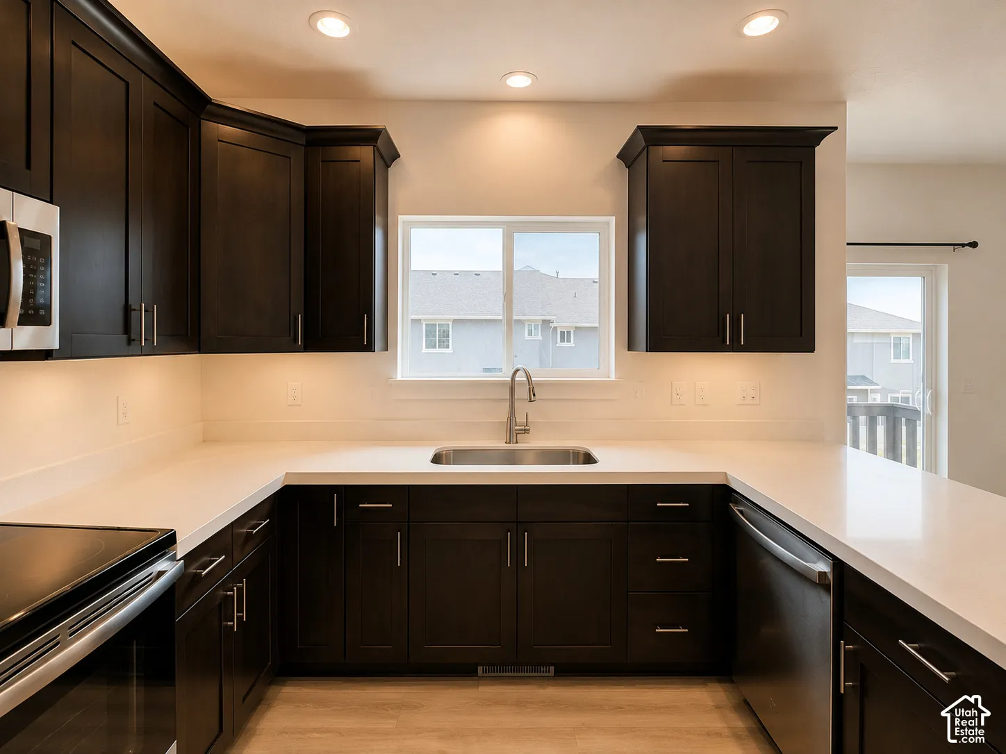 Modern kitchen featuring dark wood cabinetry, light-toned countertops, and a stainless steel undermount sink