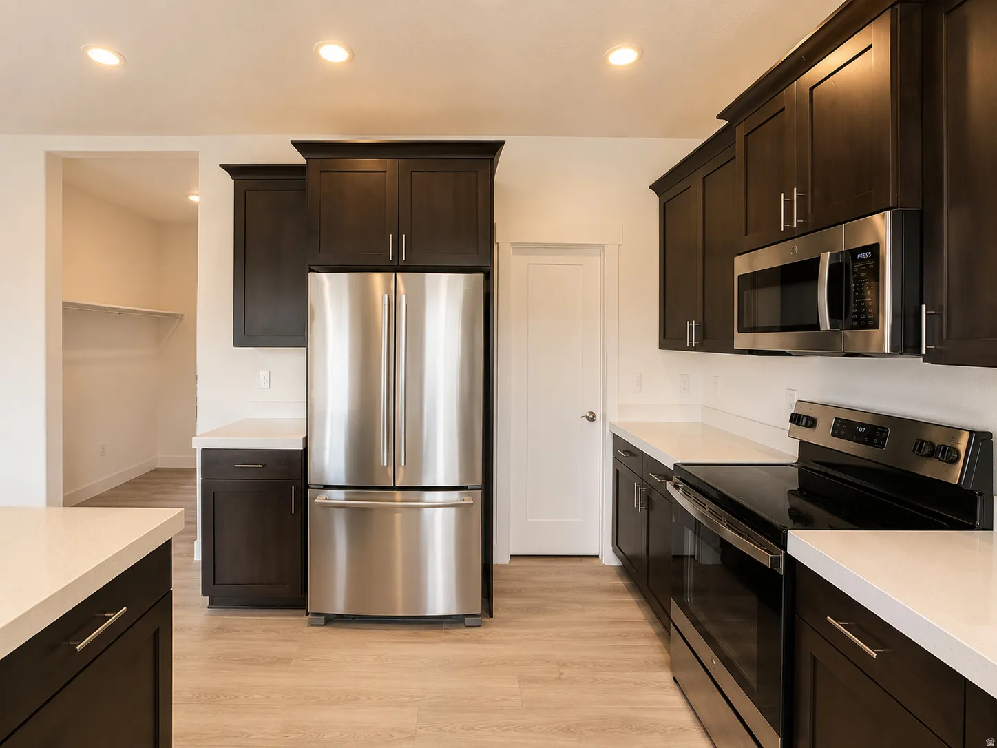 Kitchen featuring dark wood-finish cabinetry with brushed nickel hardware, white countertops, and stainless steel appliances