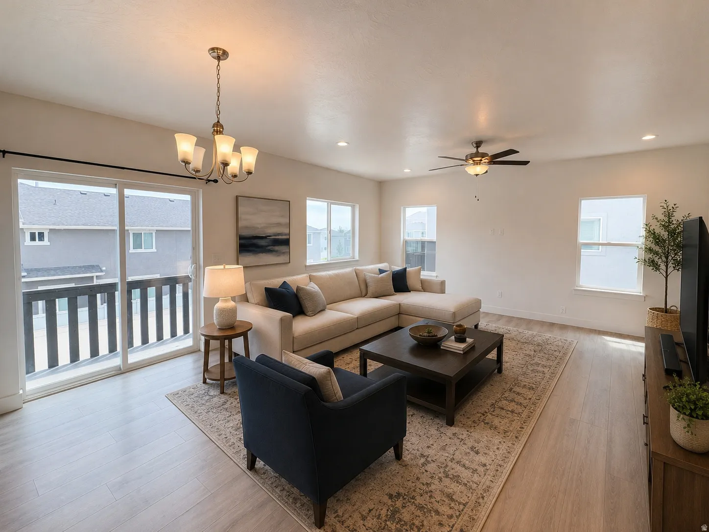 Spacious living area featuring light wood-finish flooring, a contemporary ceiling fan, recessed lighting, and a multi-light chandelier