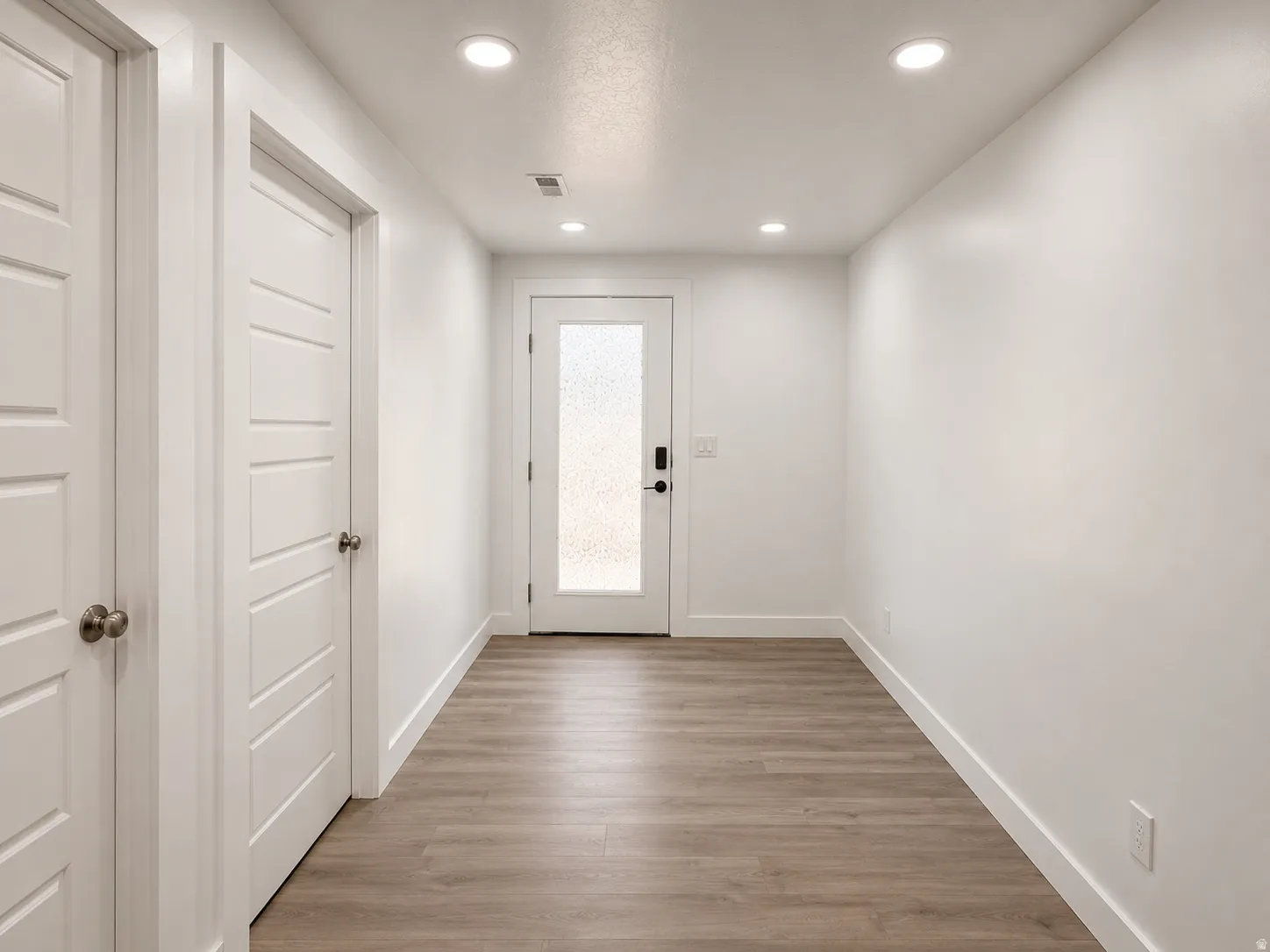 Hallway featuring wood-finish flooring, recessed lighting, and a white interior door with frosted glass paneling