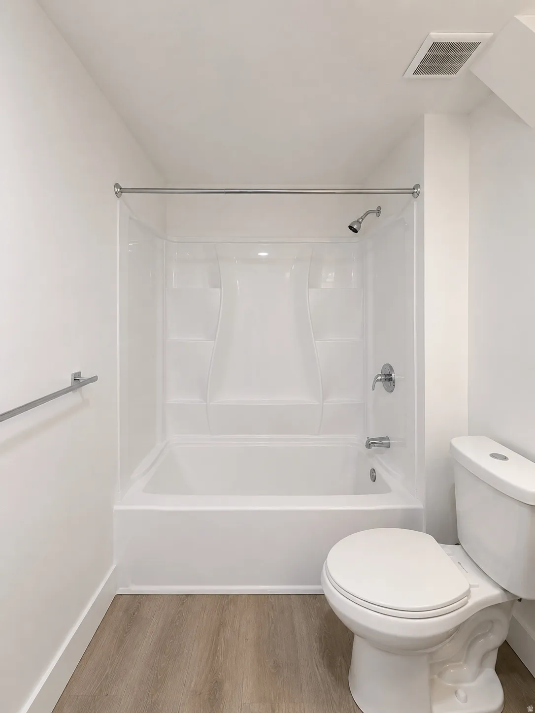 Bright bathroom featuring a white tub and shower combination with chrome fixtures, a white toilet, and wood-finish flooring